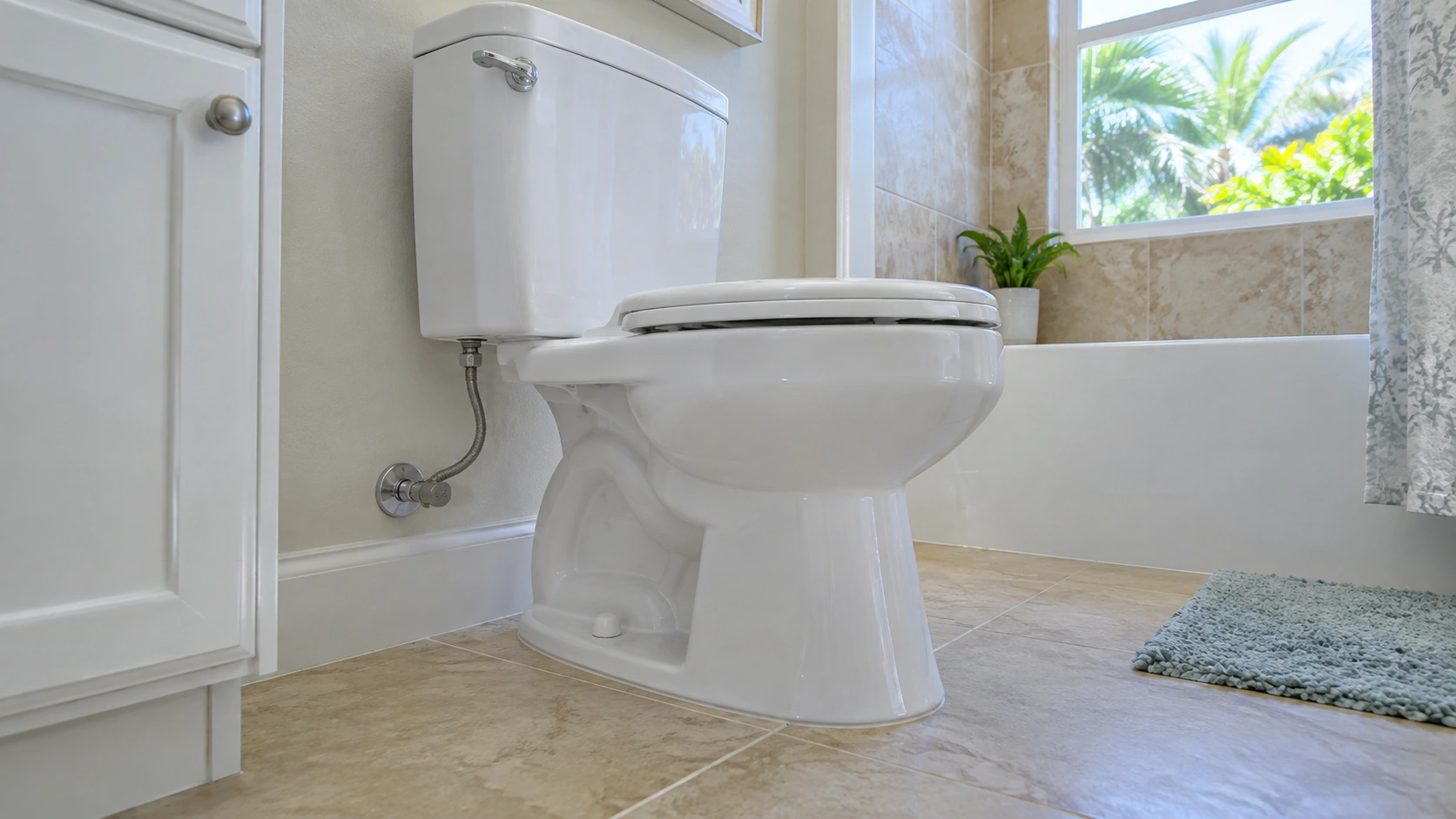 A toilet and its supply line in a bright bathroom.
